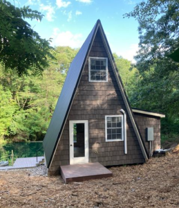 Front view of a contemporary triangular-shaped building used as a cabin getaway with wood siding sitting next to a pond