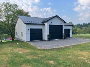 3 car detached garage with white siding, black metal roofing, and black garage doors. The garage door in the middle is larger than the 2 on both sides.